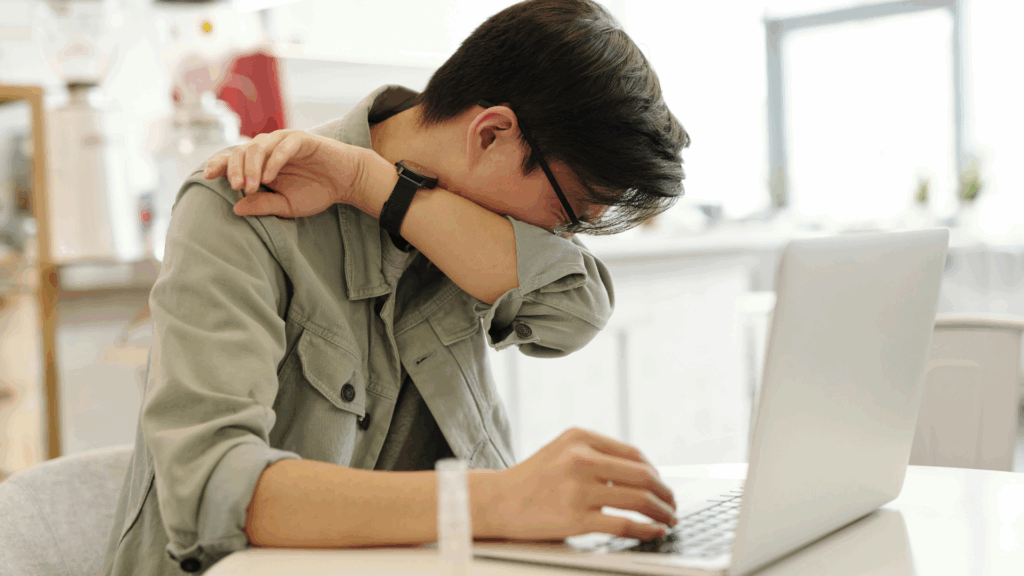 Jeune salarié malade au bureau, se couvrant la bouche en toussant