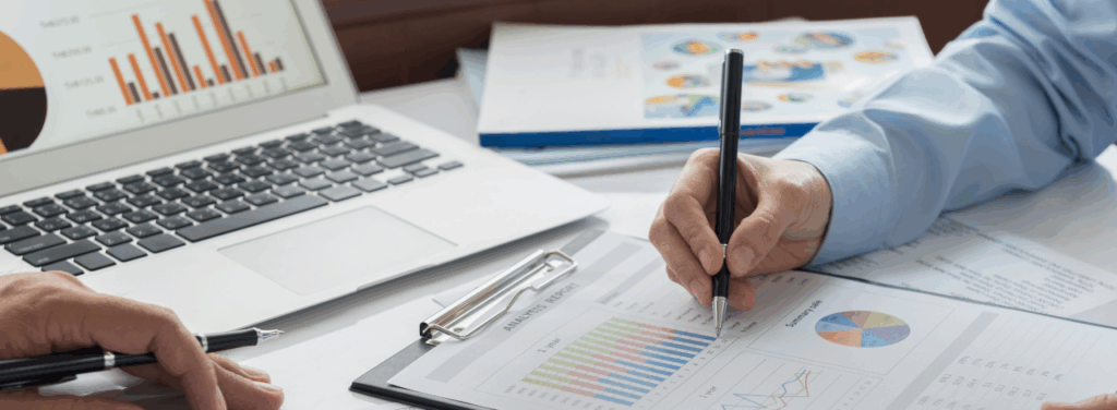 Deux professionnels analysent des graphiques financiers et des rapports comptables sur un ordinateur portable et une tablette, illustrant la gestion comptable d’une TPE et ou d'une PME.