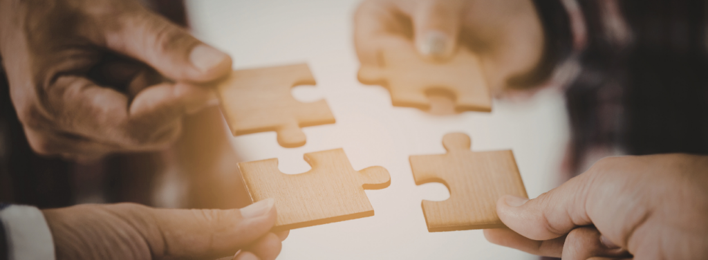 Quatre mains assemblant des pièces de puzzle en bois, représentant la collaboration et l'unité dans la gestion comptable des associations.
