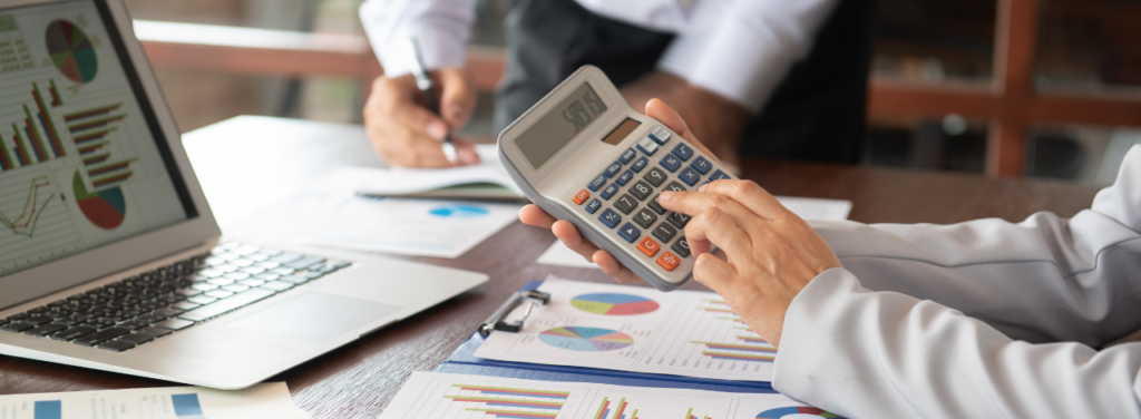 Une personne utilisant une calculatrice devant des graphiques financiers sur un ordinateur portable, illustrant la gestion comptable d'une TPE-PME.