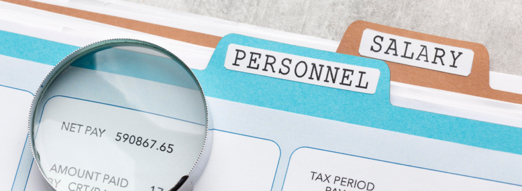 Loupe posée sur une fiche de paie, avec les mentions « Net Pay », « Personnel » et « Salary ».