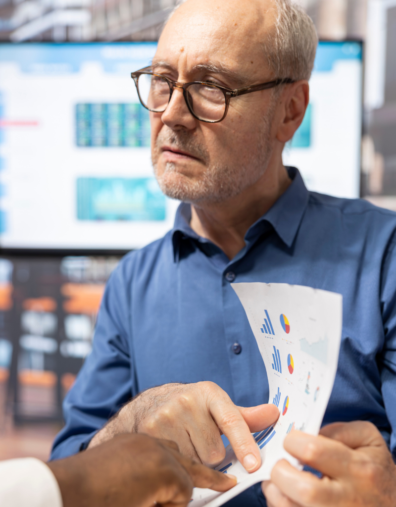 Un conseiller examine des graphiques financiers avec un porteur de projet devant plusieurs écrans de données.