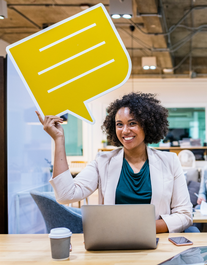 Une professionnelle devant son ordinateur tient une grande bulle de dialogue pour symboliser la communication d’entreprise.