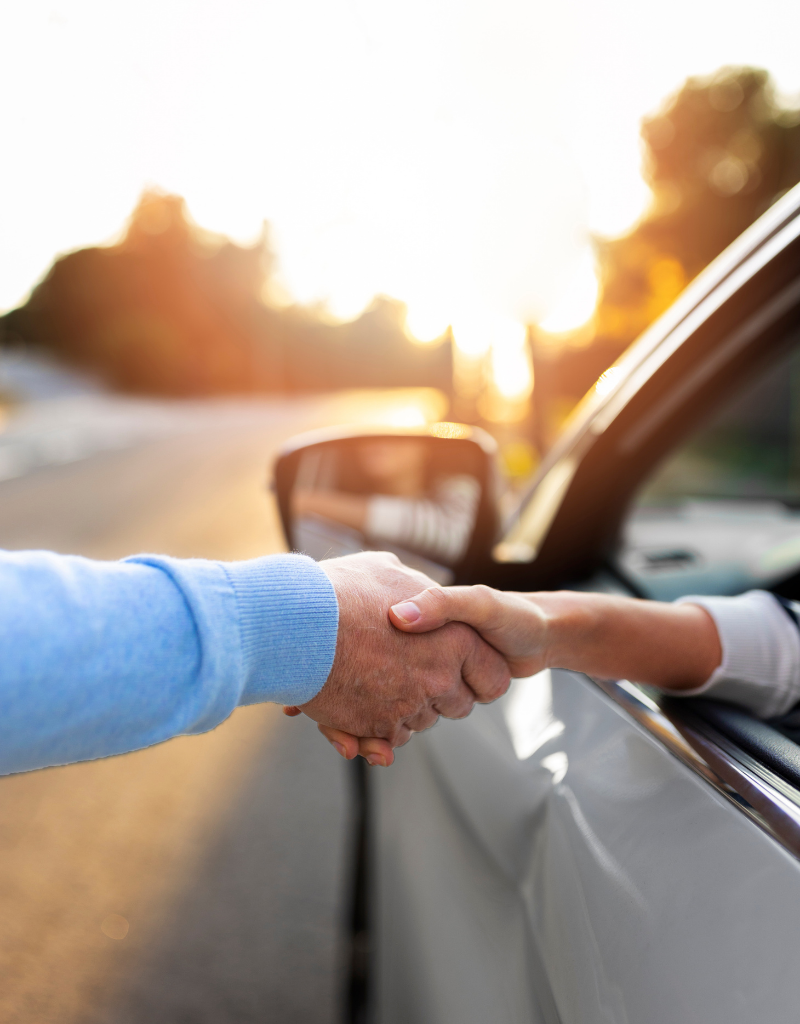 Poignée de main entre deux personnes à travers la fenêtre d’une voiture de fonction.