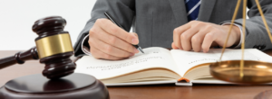 Professionnel consultant un ouvrage juridique à côté d’un marteau de juge et d’une balance de justice.